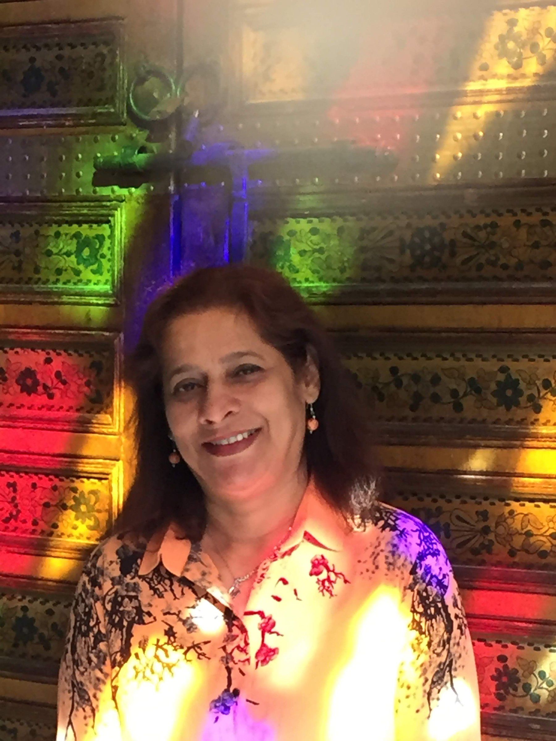 Mugdha smiling in coloured light falling through stained glass, with ornate painted panels behind her