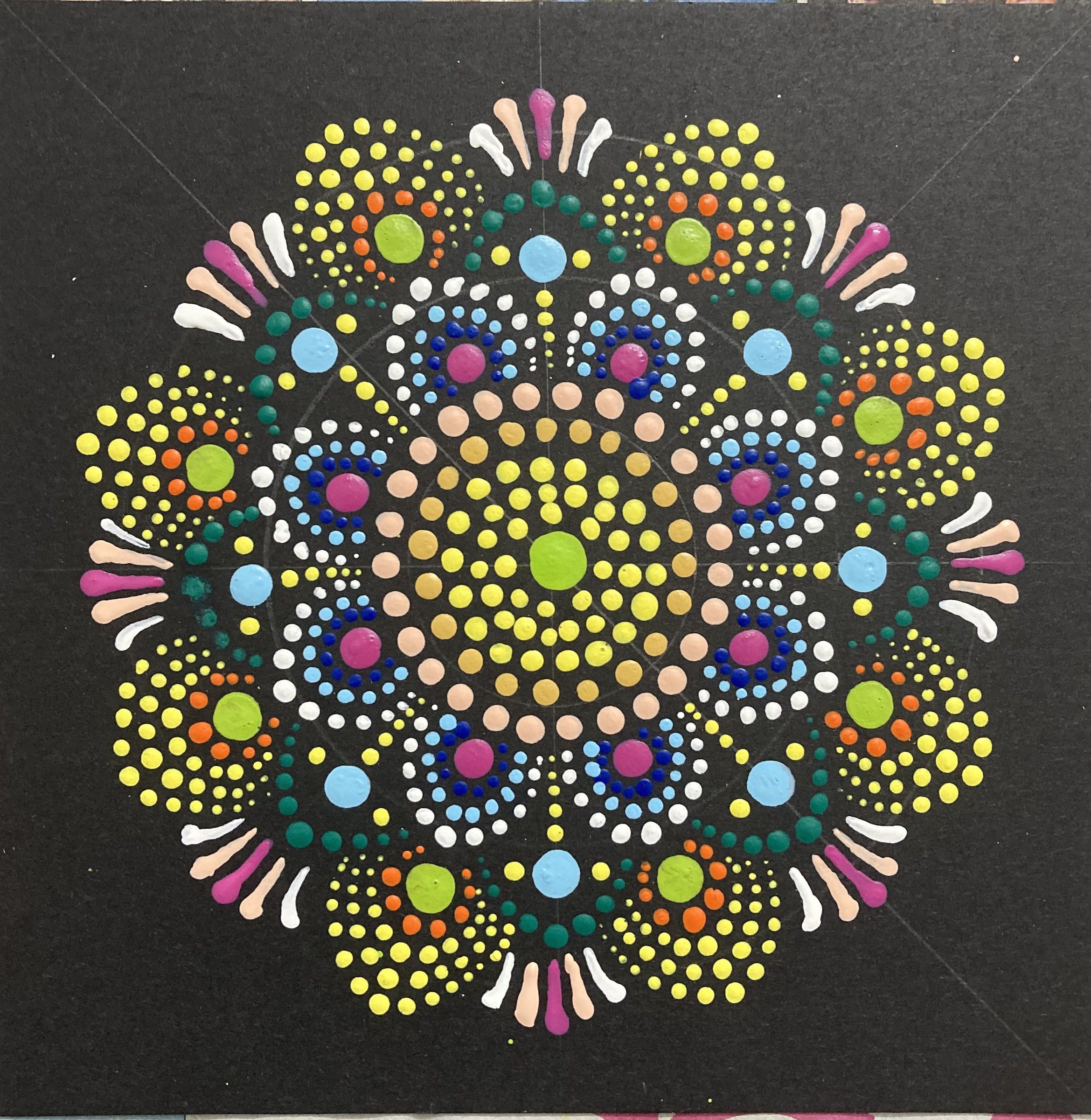 Dot-painted mandala on black, in rings of yellow, pink, blue and green dots