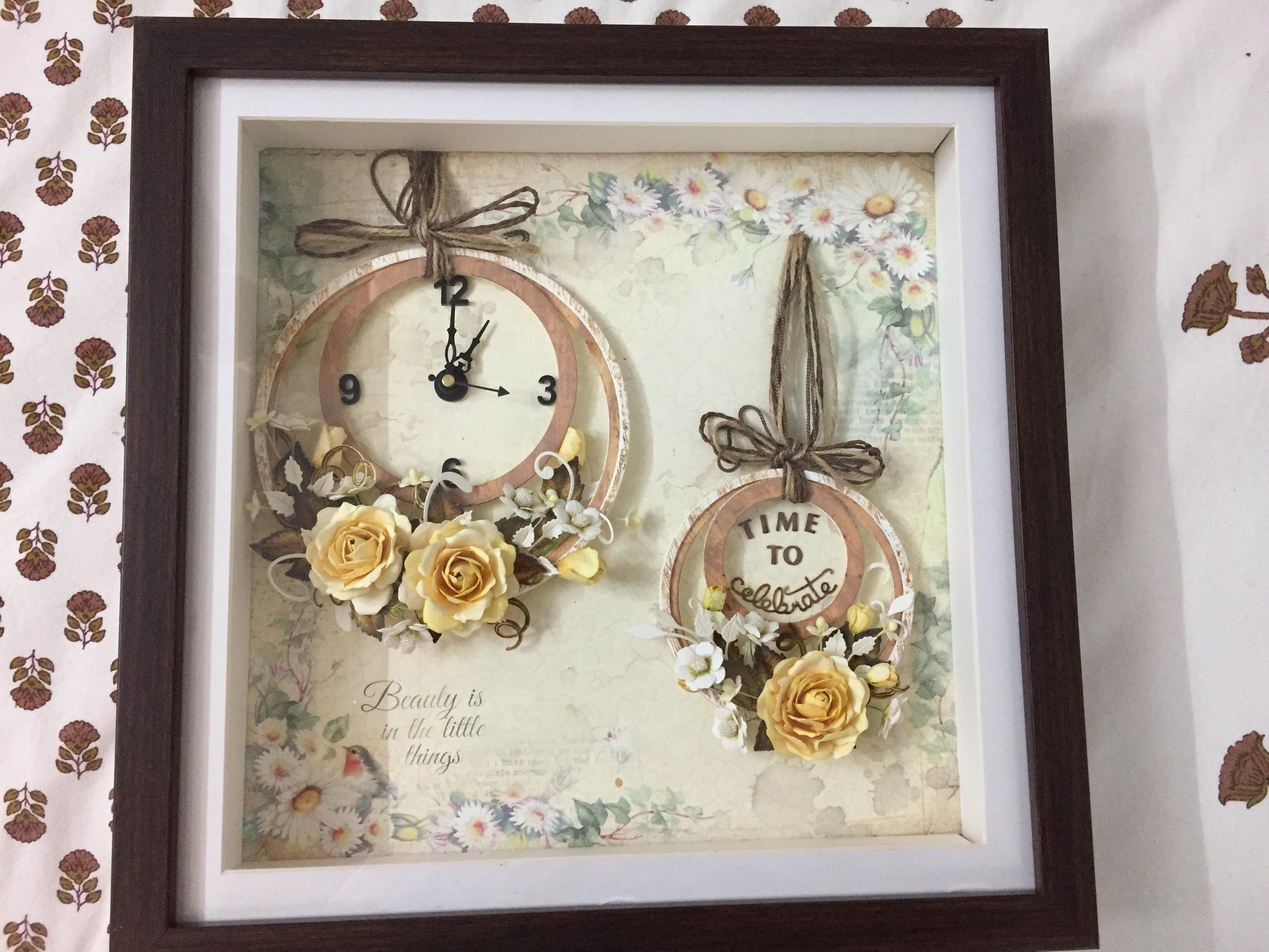 Framed shadow box with two paper clocks, one reading Time to celebrate, decorated with yellow paper roses