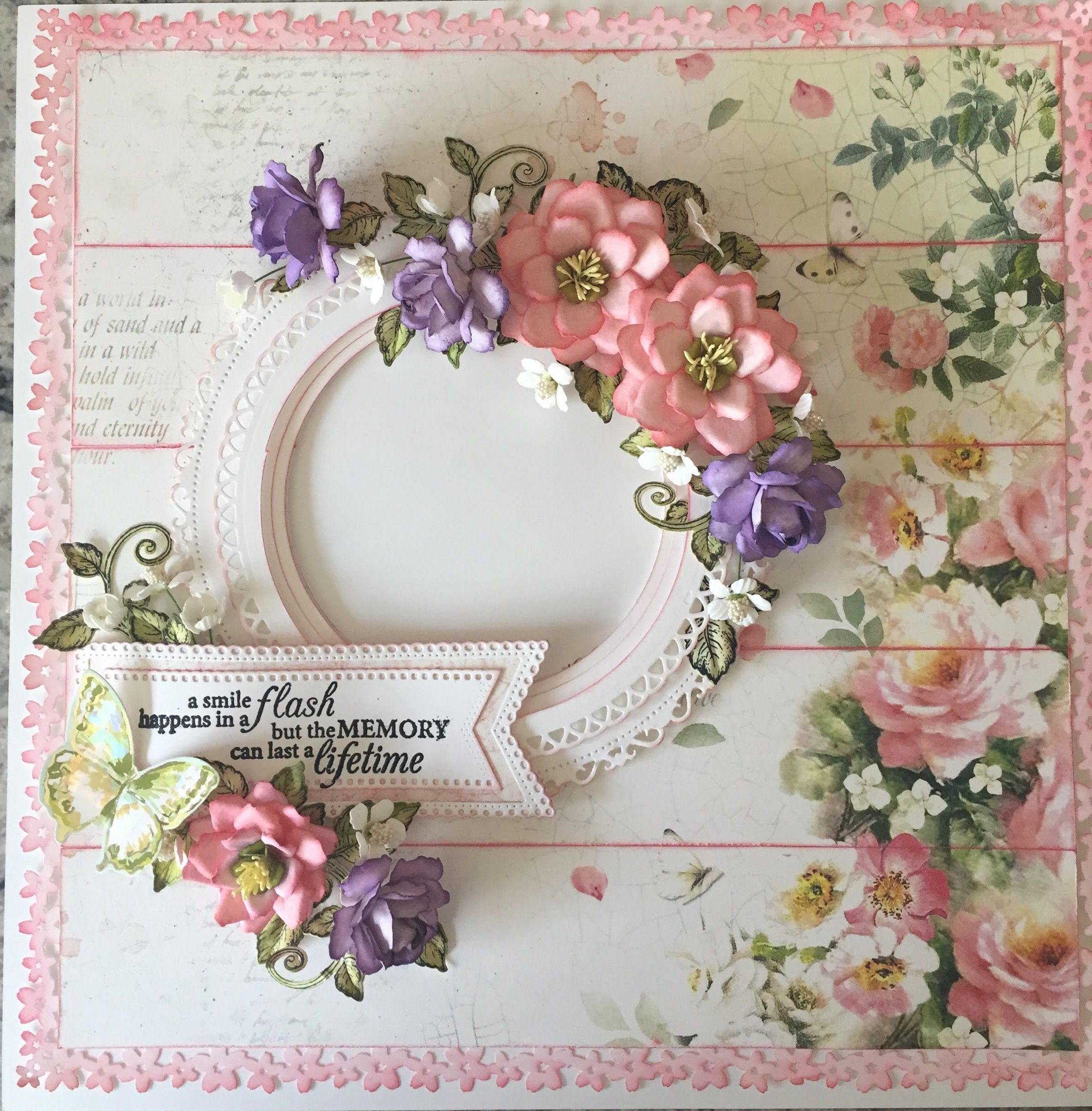 Card with pink and purple paper flowers around a white lace frame, and a banner reading a smile happens in a flash but the memory can last a lifetime