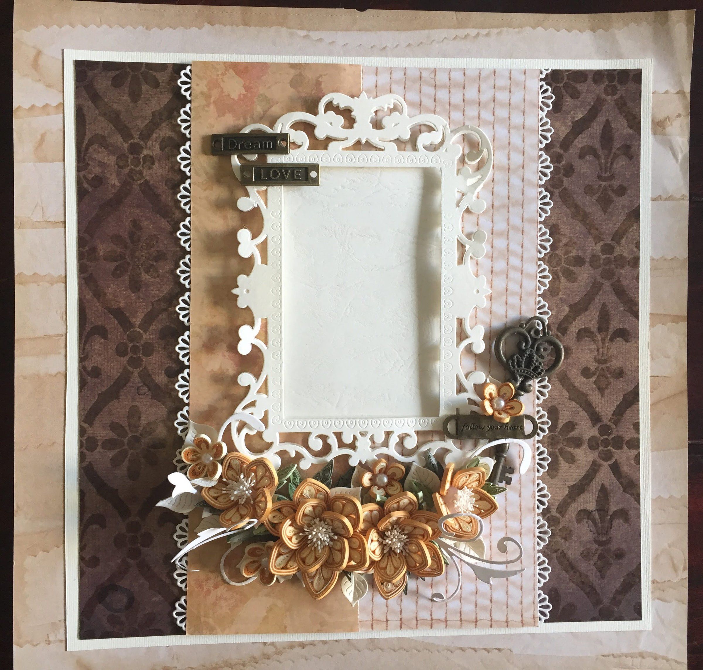 Scrapbook photo frame with a white filigree border on brown damask and peach paper, with peach paper flowers and a small key charm