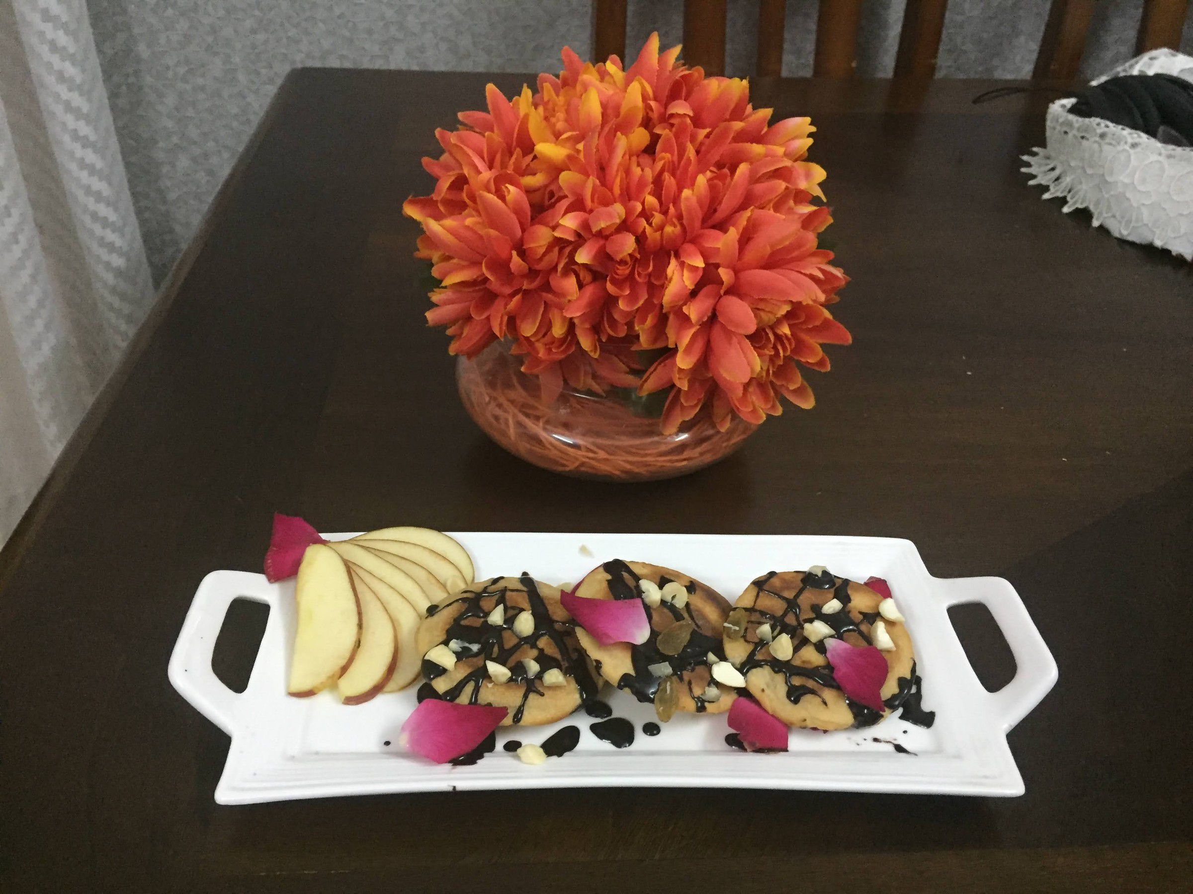 White tray of pancakes drizzled with chocolate, with apple slices and rose petals