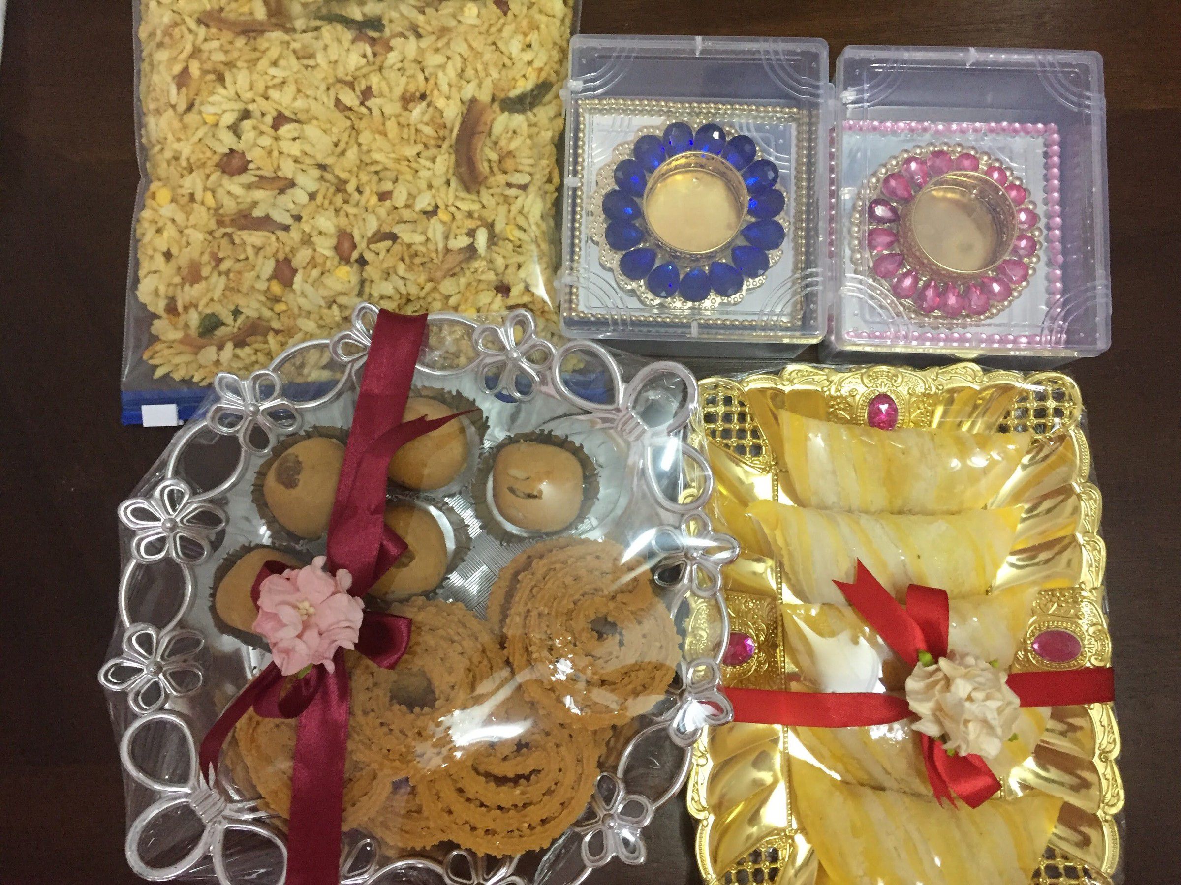 Diwali gift spread: chivda, ladoos and chakli in a ribboned silver tray, wrapped sweets on a gold tray, and jewelled diyas