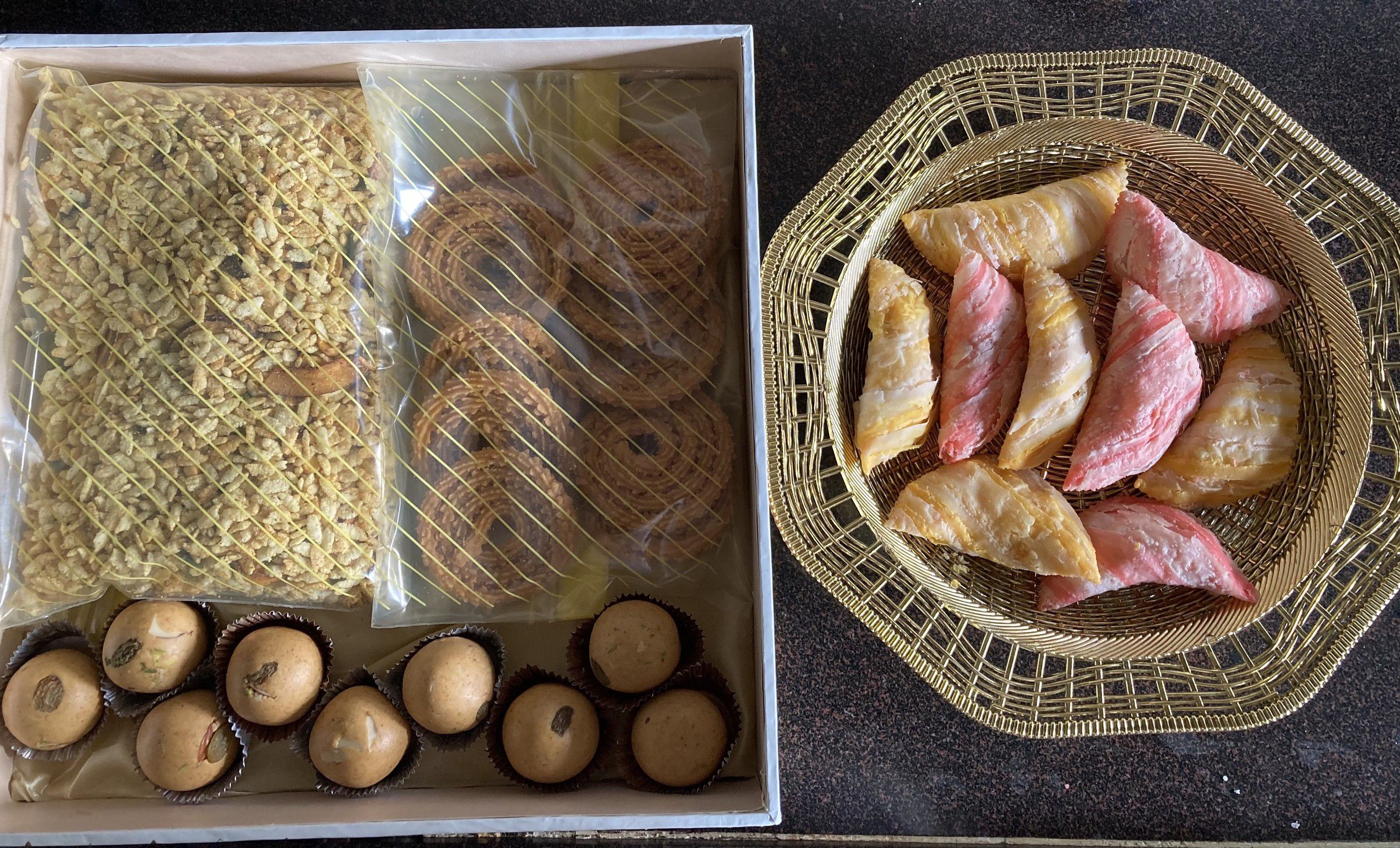 Box of chivda, chakli and ladoos beside a basket of pink and plain karanji