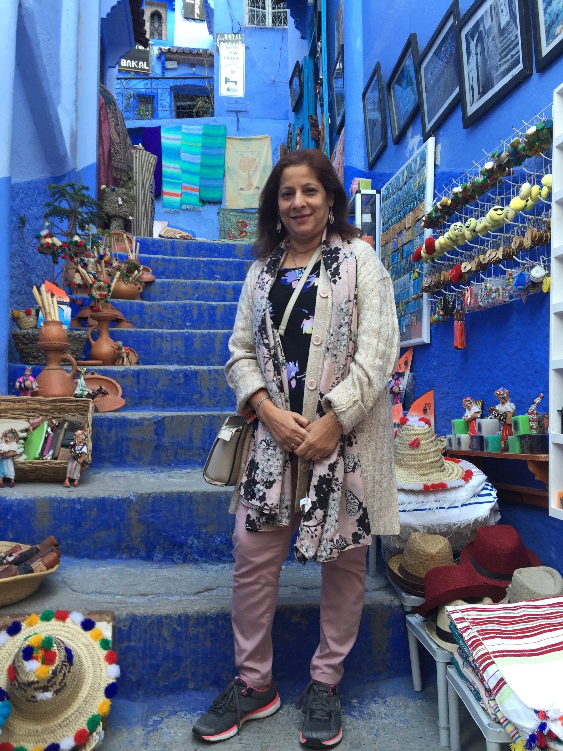 Mugdha on a blue-painted staircase lined with hats and crafts