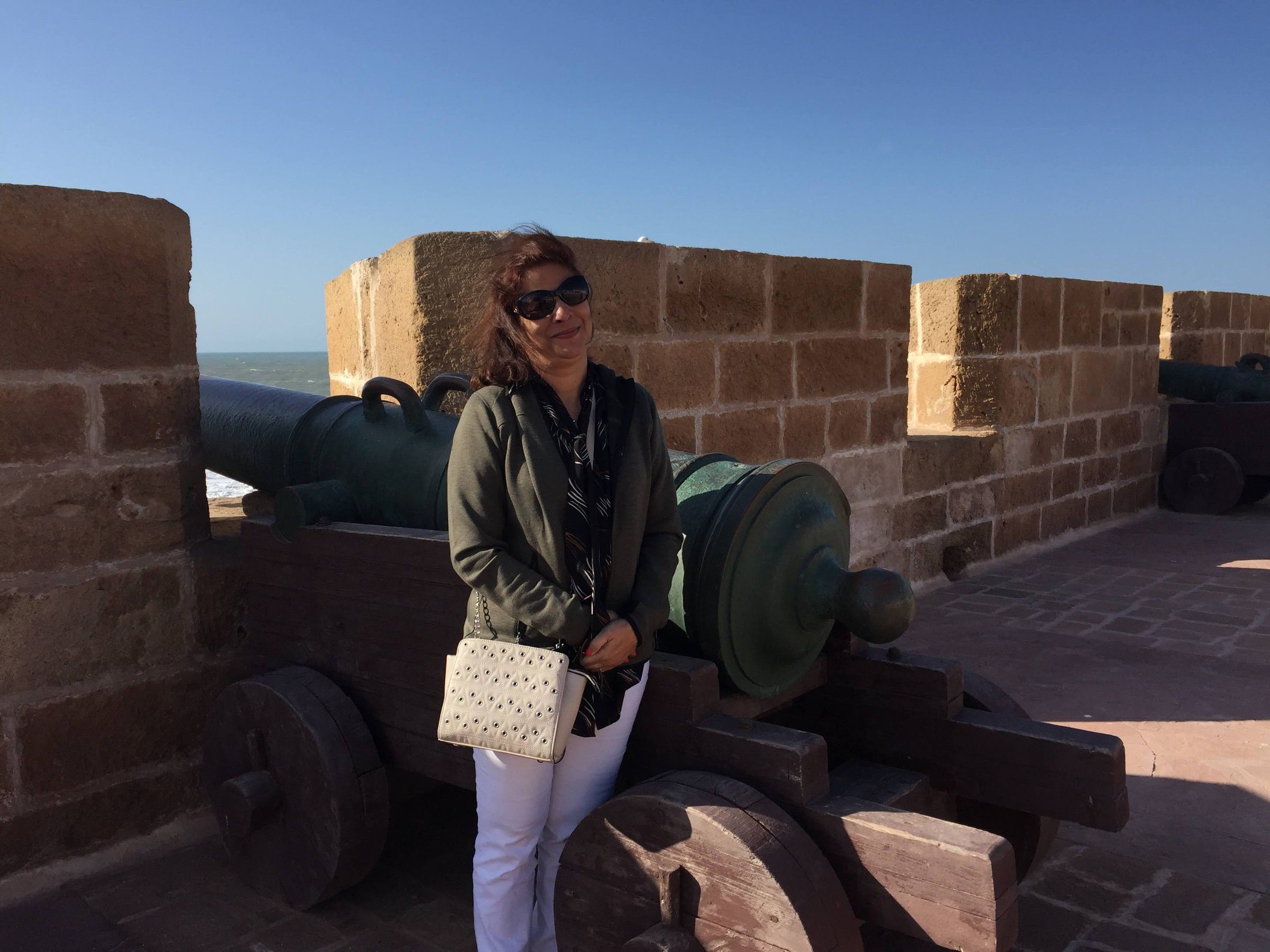 Mugdha on stone ramparts beside old bronze cannons, with the sea behind