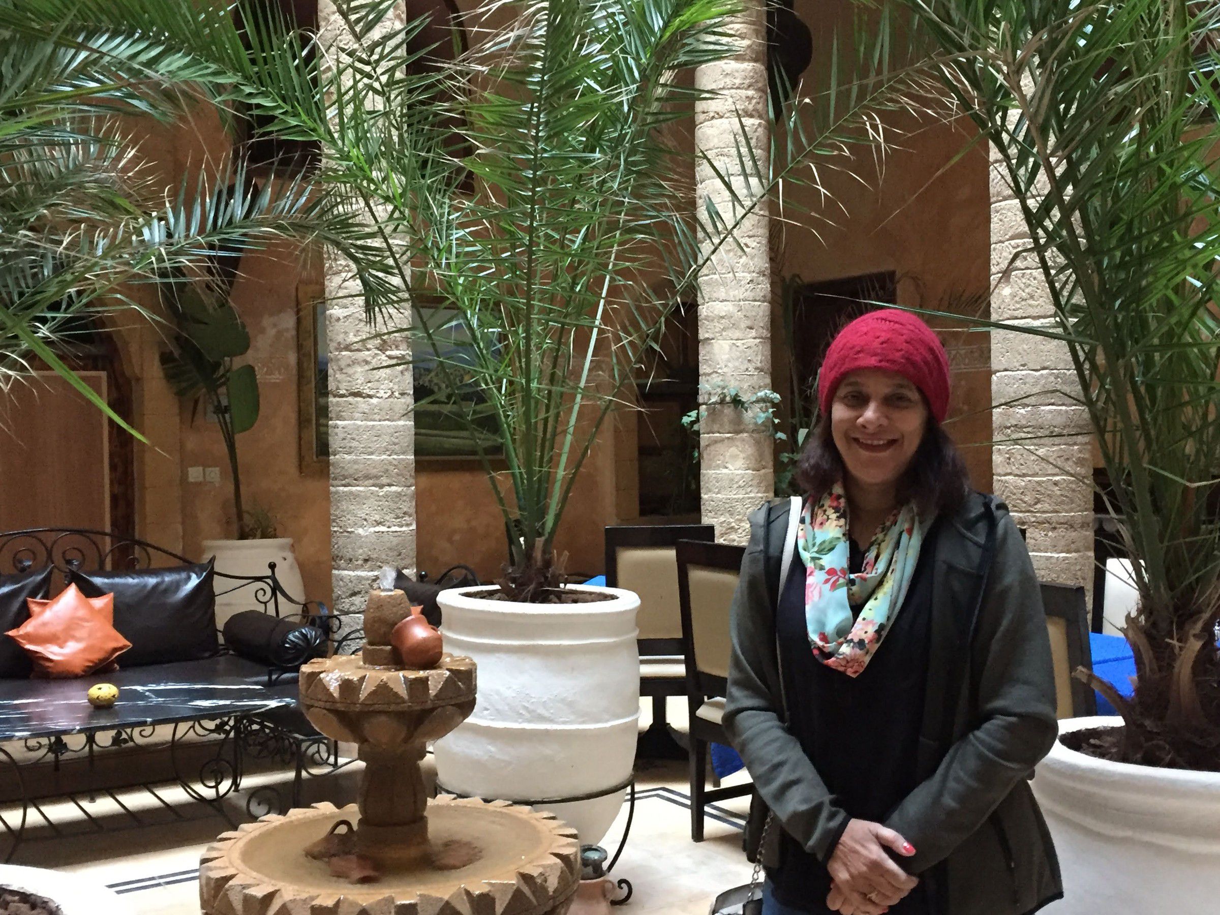 Mugdha in a red beanie in a courtyard of palms and a carved stone fountain