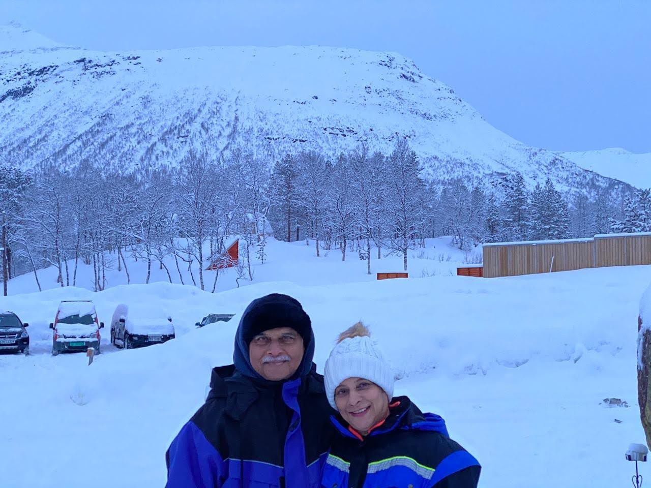 Mugdha and her husband in winter jackets in deep snow below a snow-covered mountain