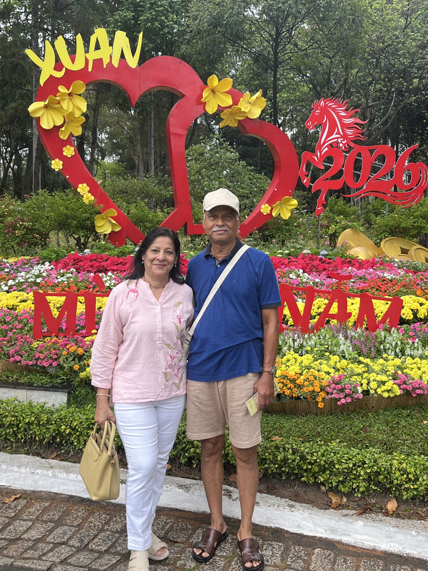 Mugdha and her husband in front of a flower display with a red heart and the words Xuân 2026
