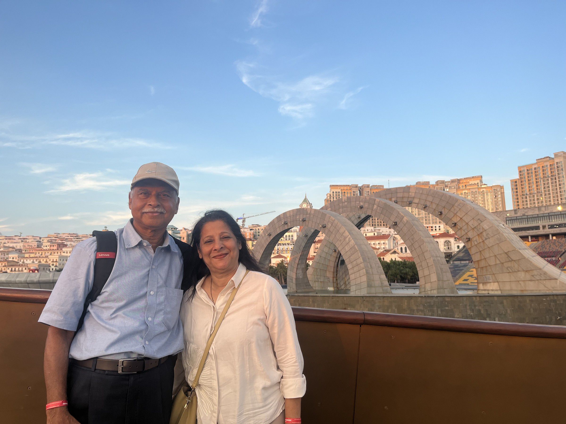 Mugdha and her husband on a terrace with stone arches, a city behind them at dusk