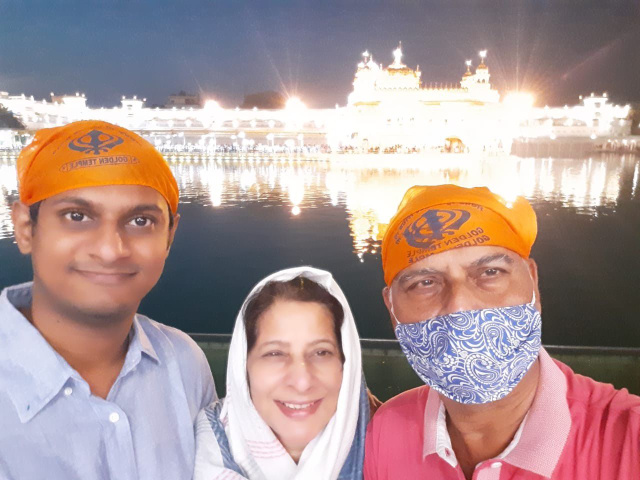 Mugdha with two family members in orange head coverings, the Golden Temple lit up behind them at night