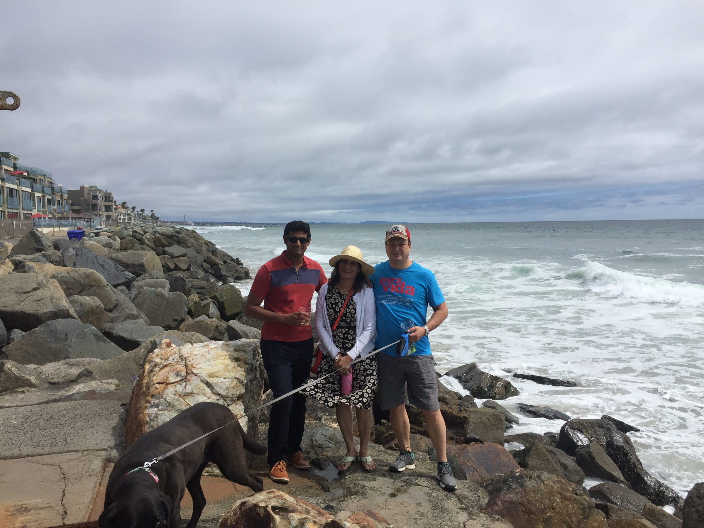 Mugdha with two men and a dog on a rocky seashore under grey skies