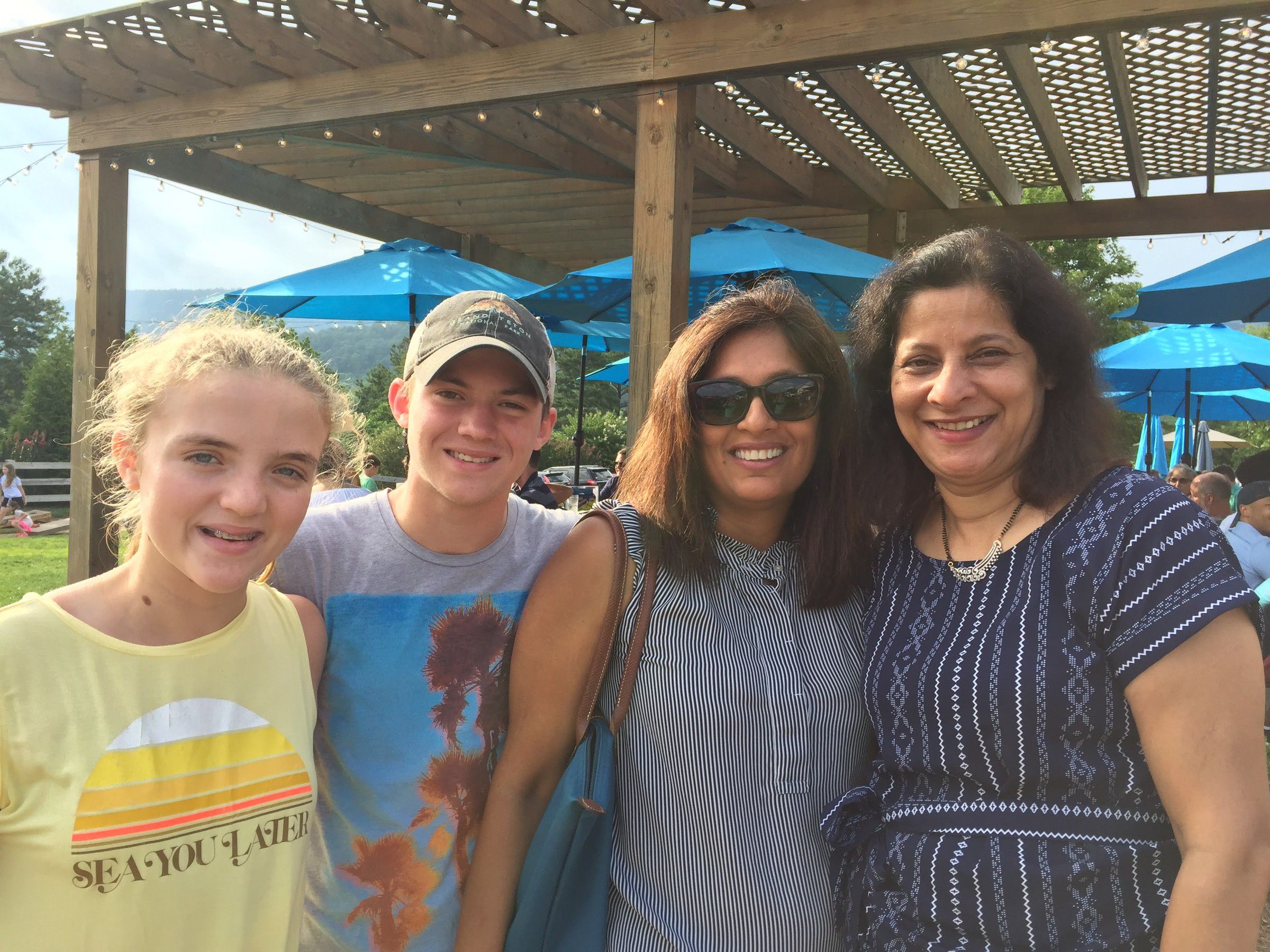 Mugdha with a woman and two teenagers under a wooden pergola with blue umbrellas